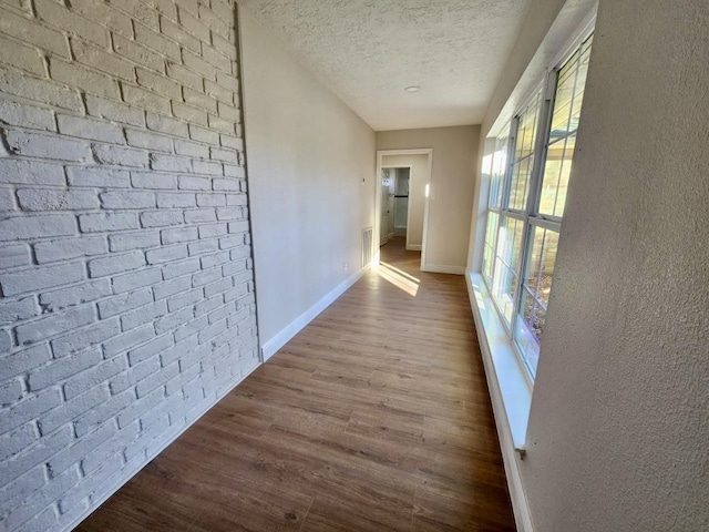 corridor featuring brick wall, a textured ceiling, and wood-type flooring