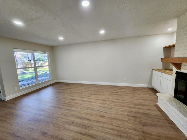 unfurnished living room featuring a textured ceiling, light wood-type flooring, and a brick fireplace