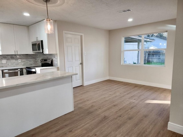 kitchen with white cabinetry, appliances with stainless steel finishes, decorative backsplash, light hardwood / wood-style flooring, and decorative light fixtures