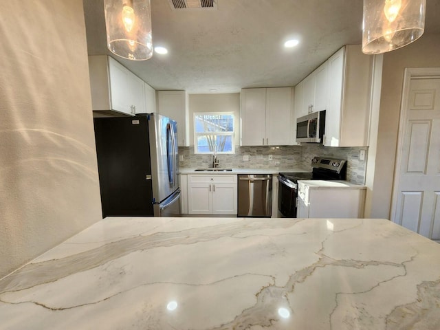 kitchen featuring stainless steel appliances, light stone countertops, white cabinets, decorative light fixtures, and sink