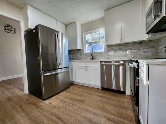 kitchen with white cabinetry, backsplash, light hardwood / wood-style flooring, and appliances with stainless steel finishes