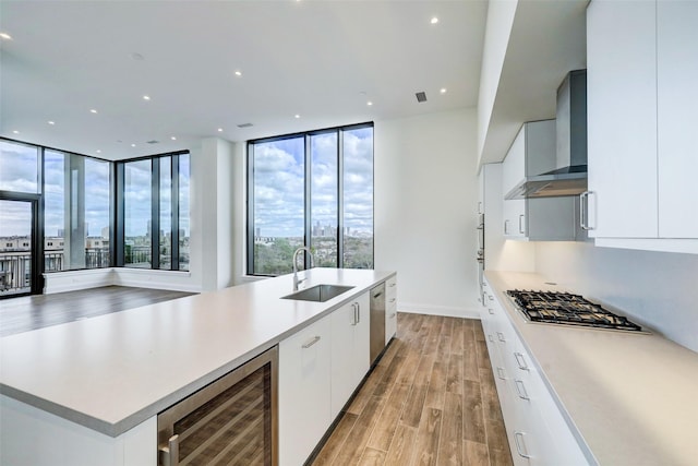 kitchen featuring stainless steel appliances, wall chimney range hood, sink, white cabinets, and wine cooler