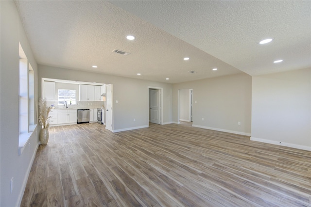 unfurnished living room with sink, a textured ceiling, and light hardwood / wood-style flooring