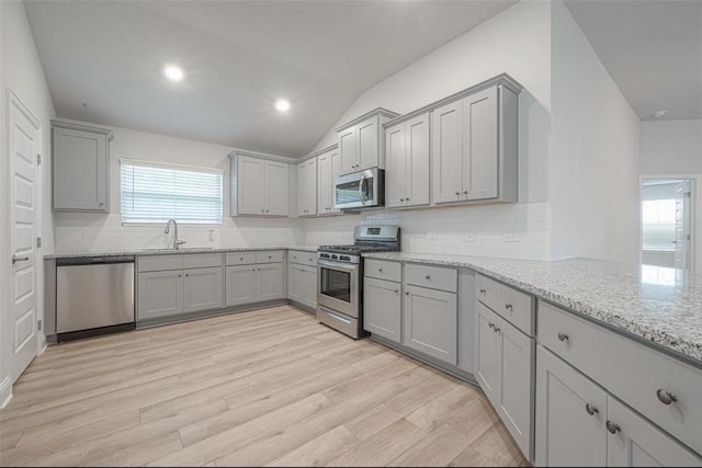 kitchen with gray cabinetry, sink, vaulted ceiling, light wood-type flooring, and stainless steel appliances