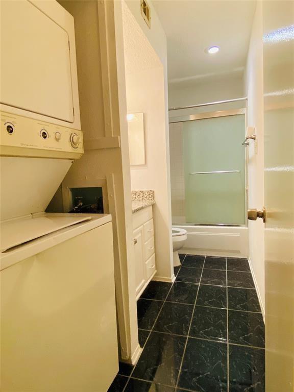 full bathroom with enclosed tub / shower combo, tile patterned floors, stacked washer and dryer, toilet, and vanity