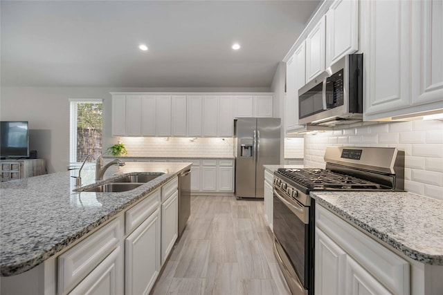 kitchen featuring white cabinets, sink, an island with sink, appliances with stainless steel finishes, and light stone counters