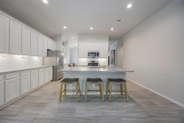 kitchen featuring light stone countertops, stainless steel appliances, white cabinetry, and a center island with sink