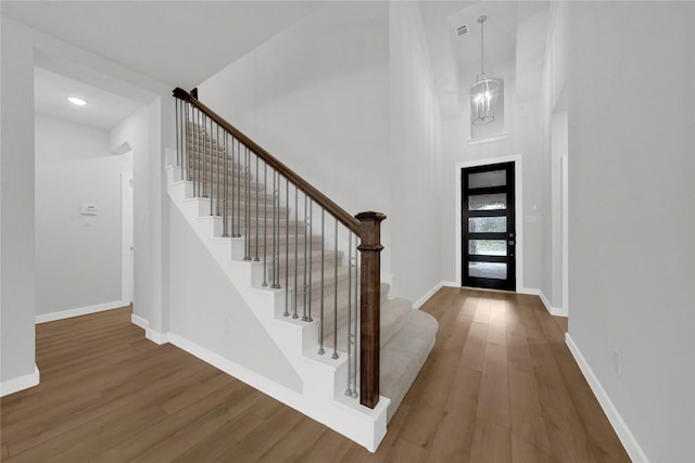 entrance foyer with hardwood / wood-style floors, a towering ceiling, and an inviting chandelier