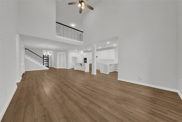 unfurnished living room with ceiling fan with notable chandelier, wood-type flooring, and a towering ceiling