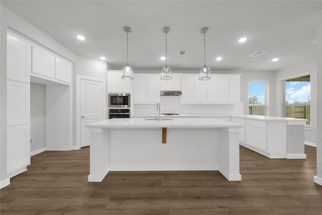 kitchen with decorative light fixtures, wall oven, a center island with sink, and backsplash