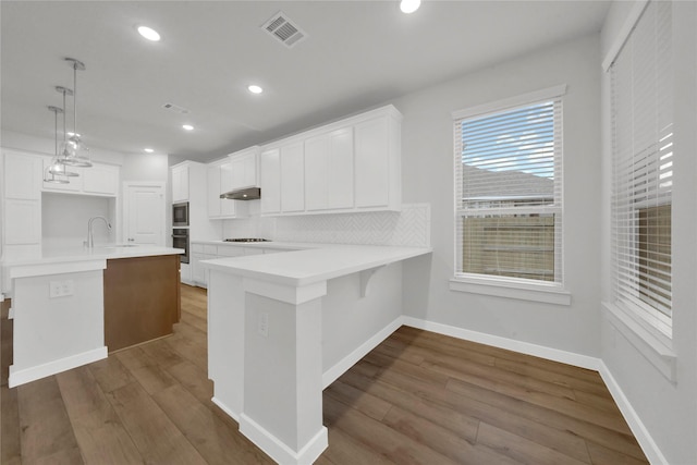 kitchen with kitchen peninsula, gas stovetop, tasteful backsplash, decorative light fixtures, and white cabinetry