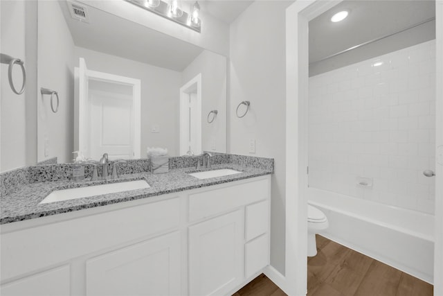 full bathroom with vanity, tiled shower / bath, wood-type flooring, and toilet