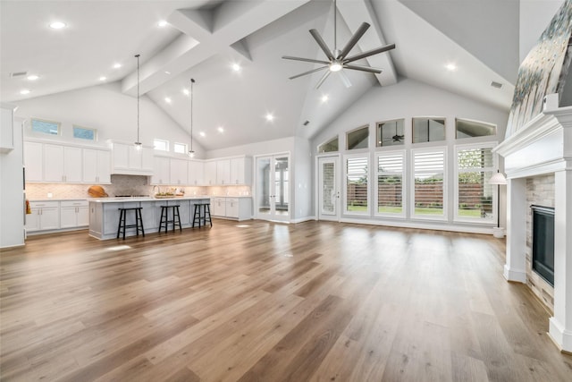 living room with a stone fireplace, high vaulted ceiling, light wood-type flooring, beamed ceiling, and ceiling fan