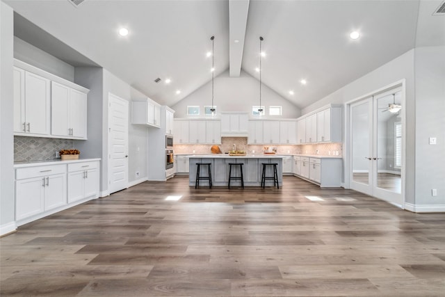 kitchen featuring hanging light fixtures, a kitchen island with sink, a breakfast bar, and white cabinets