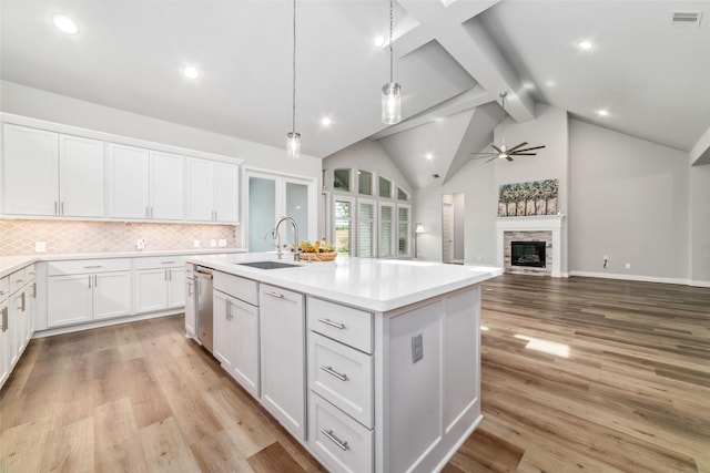 kitchen featuring a stone fireplace, sink, white cabinetry, decorative light fixtures, and an island with sink