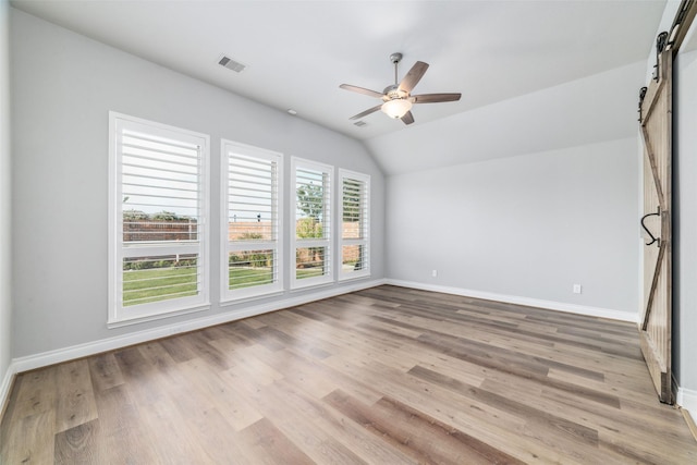 spare room featuring vaulted ceiling, a barn door, ceiling fan, and light hardwood / wood-style floors