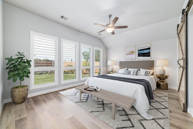 bedroom with vaulted ceiling, a barn door, ceiling fan, and light wood-type flooring