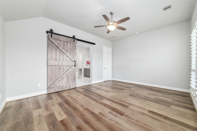 unfurnished living room with ceiling fan, a barn door, lofted ceiling, and light hardwood / wood-style floors