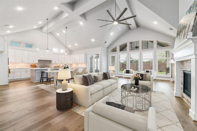 living room featuring high vaulted ceiling, a fireplace, beamed ceiling, ceiling fan, and light wood-type flooring