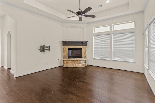 unfurnished living room with a wealth of natural light, a raised ceiling, ceiling fan, a fireplace, and dark hardwood / wood-style floors