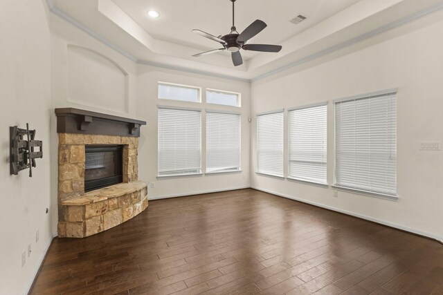 unfurnished living room with a tray ceiling, a stone fireplace, ceiling fan, and dark hardwood / wood-style flooring