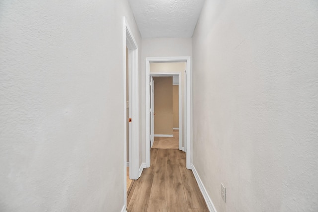 corridor with a textured ceiling and light hardwood / wood-style flooring