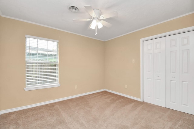 unfurnished bedroom with ceiling fan, light colored carpet, ornamental molding, and a closet