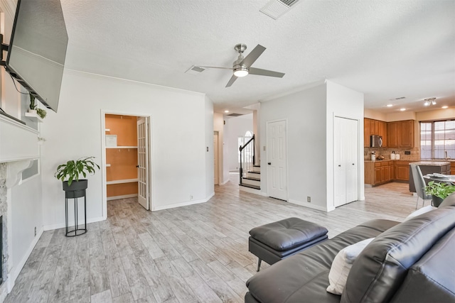 living room with a textured ceiling, ornamental molding, light hardwood / wood-style floors, and ceiling fan