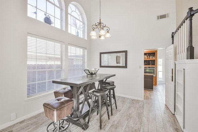 dining space featuring a towering ceiling, a chandelier, and light hardwood / wood-style floors