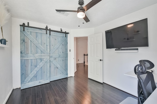 interior space with a barn door, dark wood-type flooring, a textured ceiling, and ceiling fan