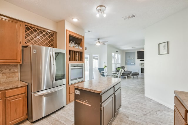 kitchen featuring ceiling fan, appliances with stainless steel finishes, backsplash, light hardwood / wood-style floors, and a kitchen island