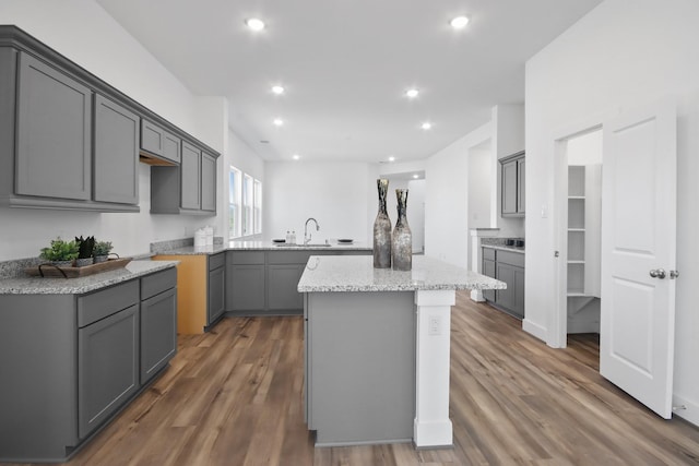 kitchen with gray cabinets, light stone counters, a center island, and dark wood-type flooring