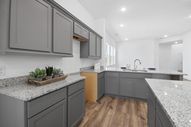 kitchen with light stone countertops, wood-type flooring, gray cabinets, and sink