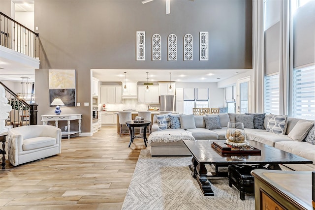 living room with a towering ceiling, light hardwood / wood-style floors, and ceiling fan