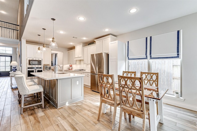 kitchen featuring appliances with stainless steel finishes, decorative light fixtures, white cabinets, light hardwood / wood-style floors, and an island with sink