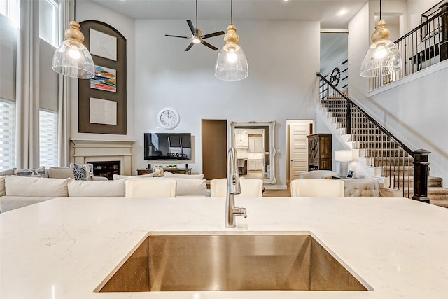 kitchen with light stone counters, sink, ceiling fan, and hanging light fixtures