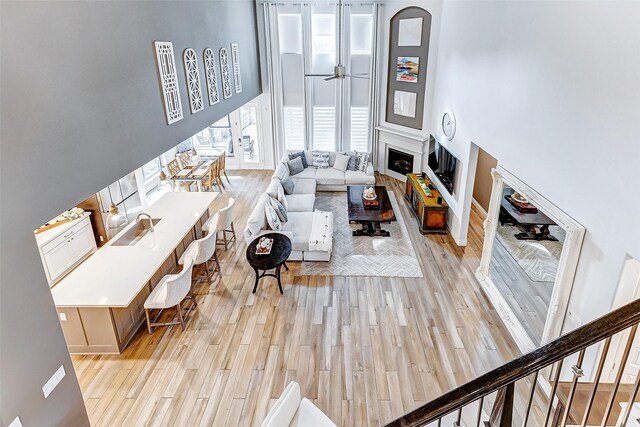 living room featuring ceiling fan, sink, a high ceiling, and light wood-type flooring