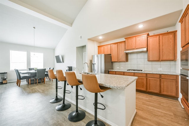 kitchen featuring a breakfast bar, stainless steel appliances, a kitchen island with sink, sink, and hanging light fixtures