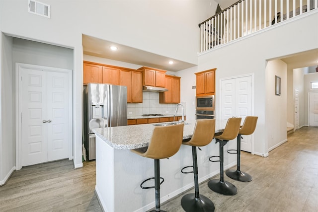 kitchen featuring decorative backsplash, appliances with stainless steel finishes, a kitchen bar, sink, and an island with sink