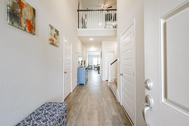 foyer entrance featuring a towering ceiling, a ceiling fan, light wood-style flooring, and stairs