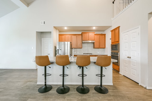 kitchen with stainless steel appliances, backsplash, a towering ceiling, a breakfast bar area, and a kitchen island with sink