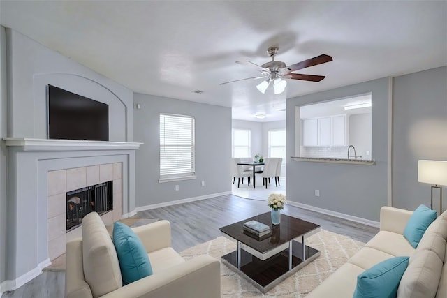 living room featuring ceiling fan, a fireplace, and light hardwood / wood-style flooring