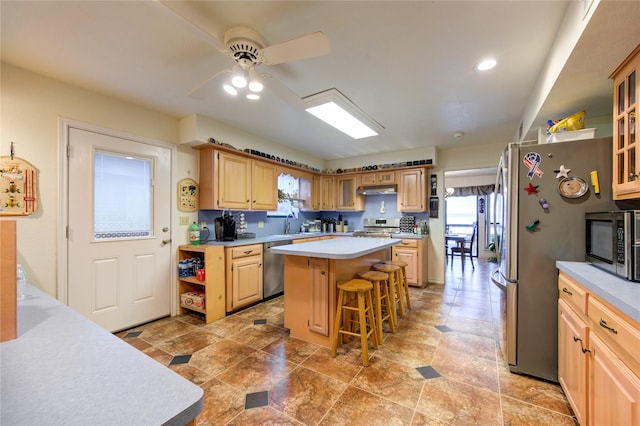 kitchen featuring stainless steel appliances, ceiling fan, light brown cabinets, a center island, and a breakfast bar area