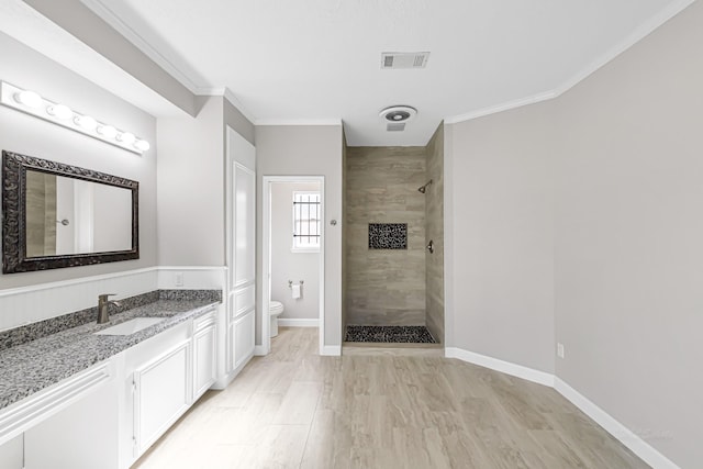 bathroom featuring a tile shower, vanity, ornamental molding, and toilet