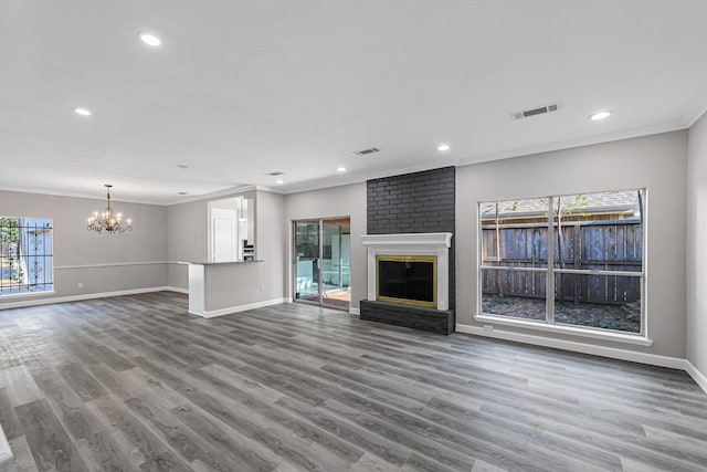 unfurnished living room featuring a chandelier, wood-type flooring, a brick fireplace, and plenty of natural light