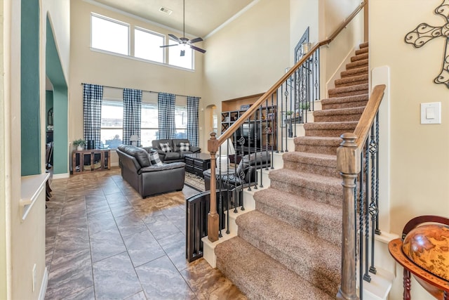 stairway featuring a high ceiling, ceiling fan, and crown molding