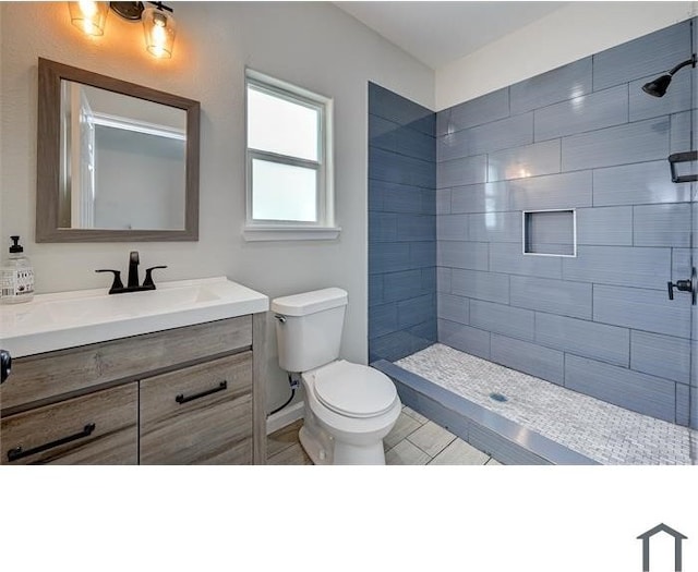 bathroom with a tile shower, vanity, and toilet