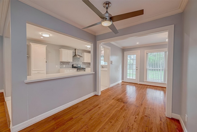 kitchen with gas stove, white cabinetry, wall chimney exhaust hood, backsplash, and light wood-type flooring