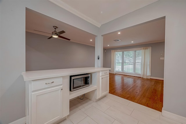 unfurnished living room featuring ceiling fan, light tile patterned floors, built in desk, and ornamental molding