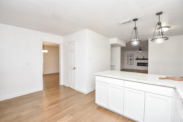 kitchen with light stone countertops, white cabinetry, hanging light fixtures, and light wood-type flooring